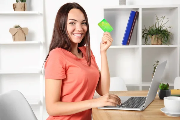 Mujer joven usando el ordenador portátil mientras sostiene la tarjeta de crédito en casa. Concepto de compras por Internet — Foto de Stock