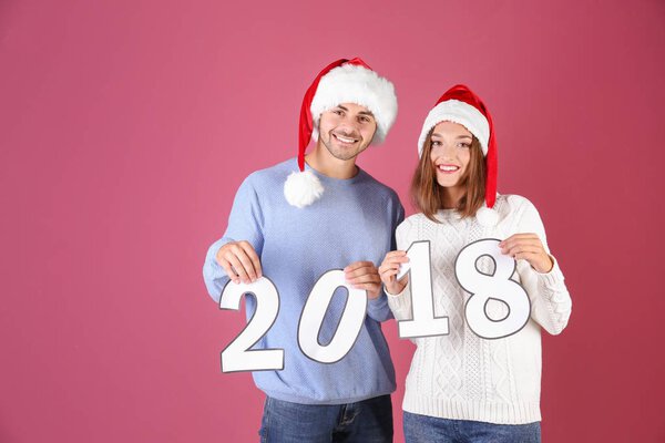 Young couple with paper figures 2018 on color background. Christmas celebration concept