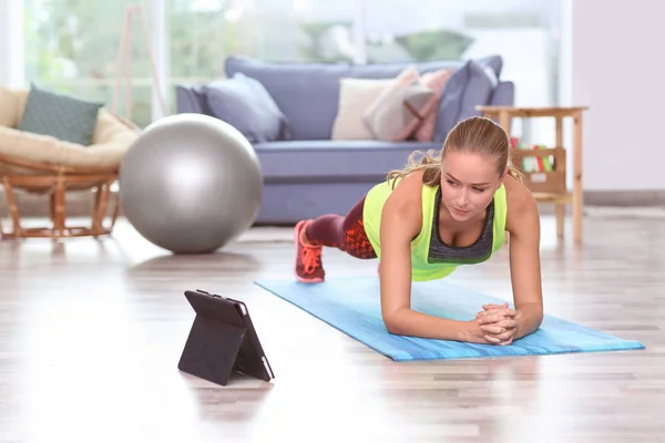 Jovem mulher esportiva com tablet praticando ioga em casa — Fotografia de Stock