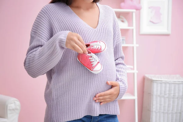 Wanita hamil memegang sepatu bayi di rumah — Stok Foto