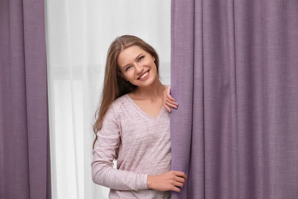 Jovem mulher de pé perto de cortinas em casa — Fotografia de Stock