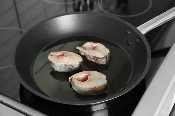 Frying pan with raw fish steaks on stove in kitchen — Stock Photo, Image