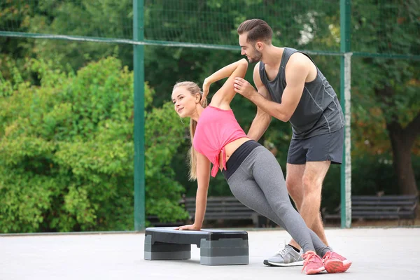 Mujer joven haciendo ejercicio con entrenador personal en el campo de deportes —  Fotos de Stock
