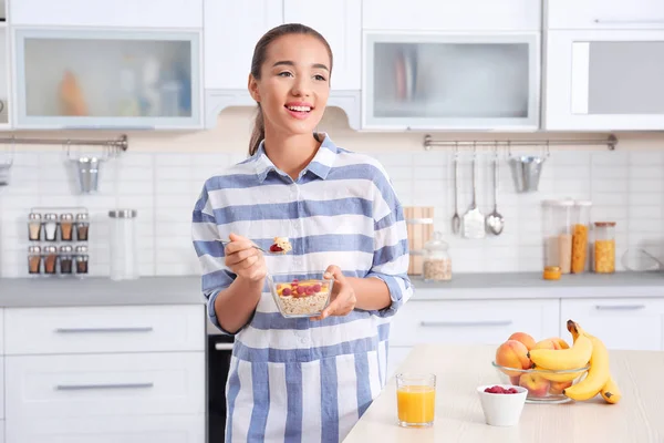 Молодая женщина в пижаме ест овсянку на кухне — стоковое фото