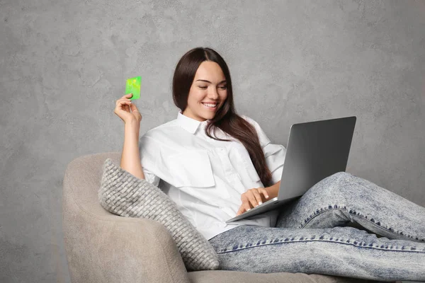 Mladá žena pomocí přenosného počítače podržíte kreditní kartu na šedém pozadí. Internetové nákupní koncept — Stock fotografie