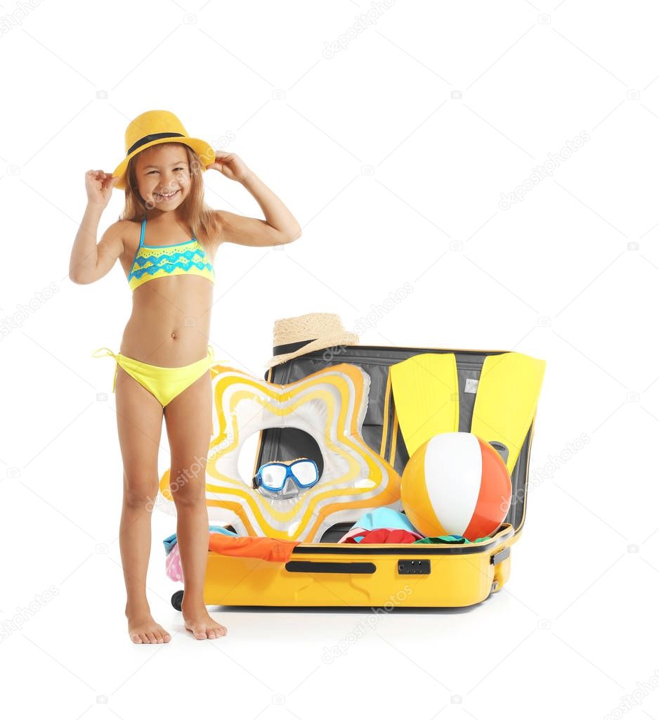 Adorable little girl in swimsuit near suitcase on white background