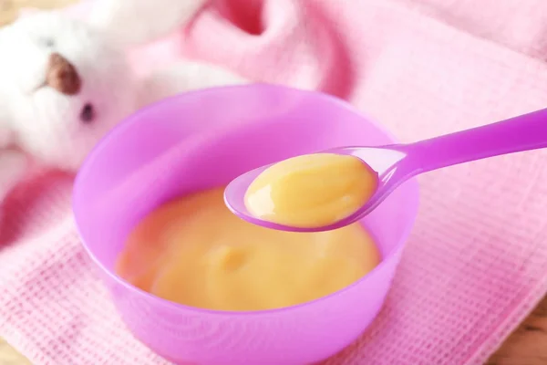 Plastic spoon and bowl with baby food — Stock Photo, Image