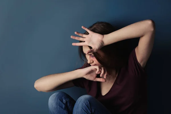 Battered young woman sitting on color background — Stock Photo, Image