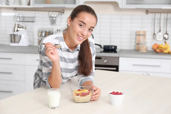Mladá žena v pyžamu jíst ovesné vločky v kuchyni — Stock fotografie