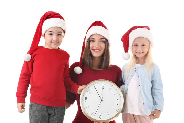 Mujer joven y niños lindos en sombreros de Santa con reloj sobre fondo blanco. Concepto de cuenta atrás de Navidad — Foto de Stock