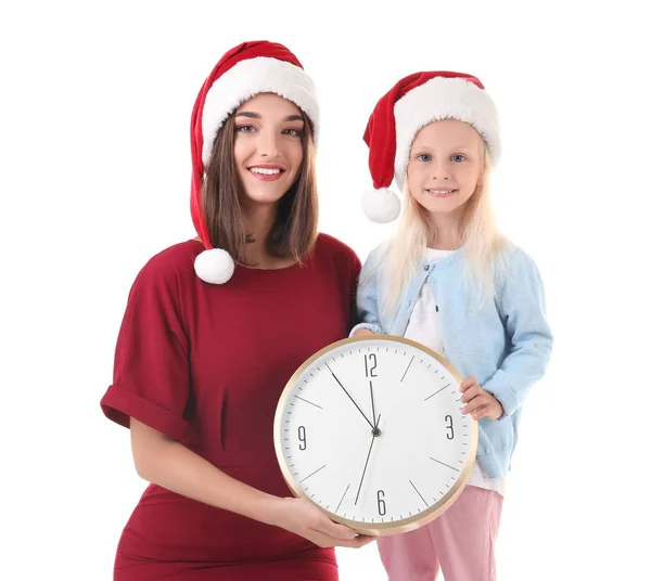 Jonge vrouw en schattig meisje in Santa hoeden met klok op witte achtergrond. Christmas countdown concept — Stockfoto