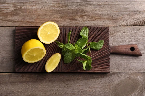 Cutting board with mint and lemon on wooden background — Stock Photo, Image