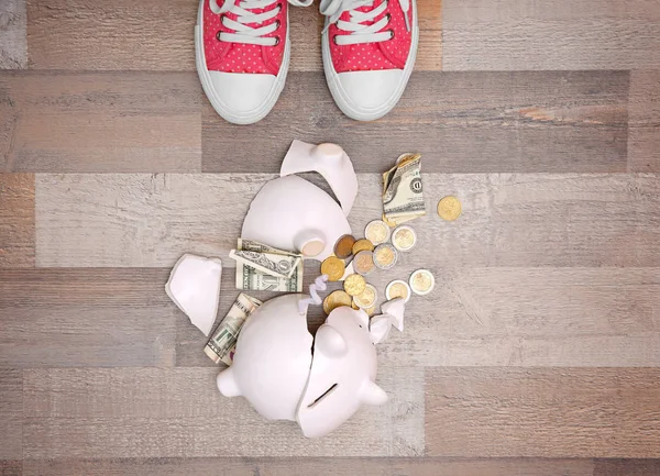 Woman standing near broken piggy bank with money on floor — Stock Photo, Image