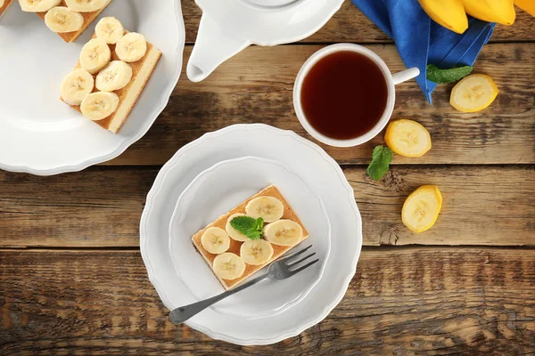 Plate with tasty banana cake and cup of tea on wooden table — Stock Photo, Image