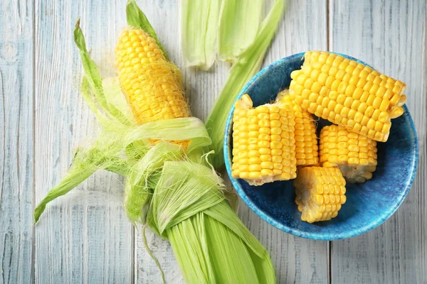 Schüssel und frische Maiskolben auf Holztisch — Stockfoto