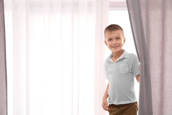 เด็กน่ารักยืนอยู่ใกล้หน้าต่างกับม่านที่สวยงามในร่ม — ภาพถ่ายสต็อก