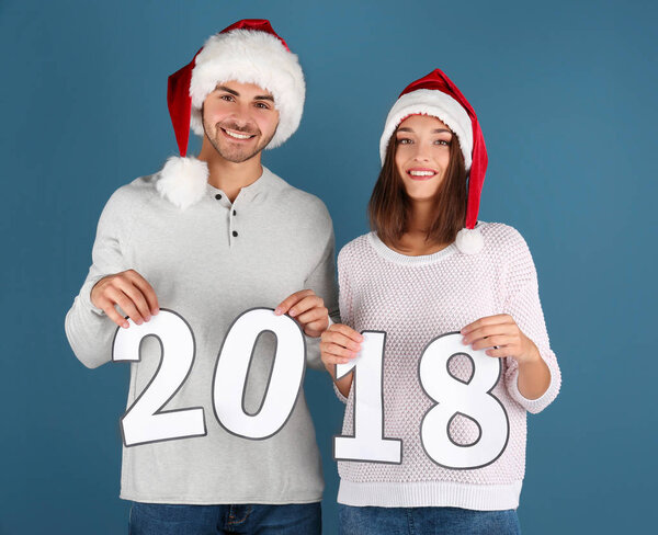 Young couple with paper figures 2018 on color background. Christmas celebration concept