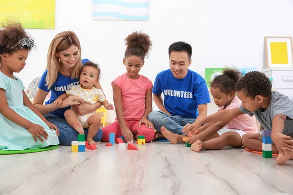 Young volunteers playing with little children in light room. Volunteering abroad concept — Stock Photo, Image