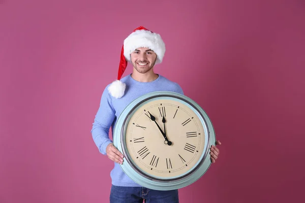 Jeune homme en chapeau de Père Noël avec horloge sur fond de couleur. Concept de compte à rebours de Noël — Photo
