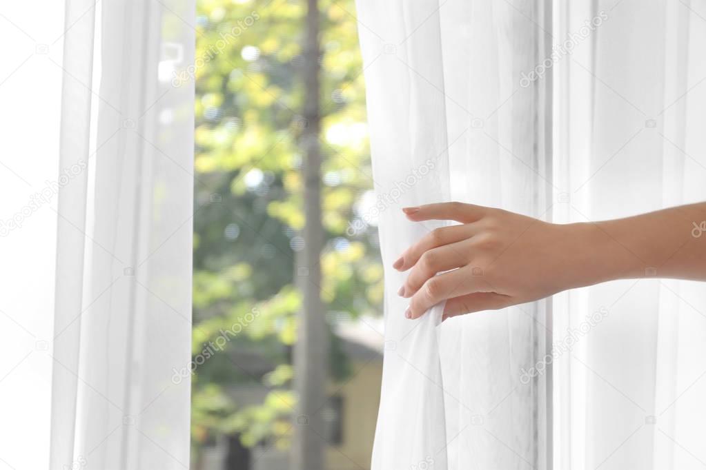 Woman opening white curtains