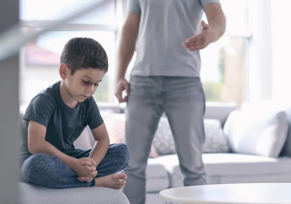 Kleiner Junge mit blauen Flecken im Gesicht und Mann im Hintergrund. Konzept zur häuslichen Gewalt — Stockfoto