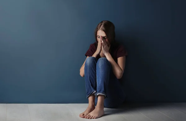 Mulher jovem agredida sentada perto da parede azul — Fotografia de Stock