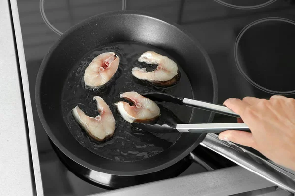 Женщина жарит рыбные стейки на кастрюле на кухне — стоковое фото