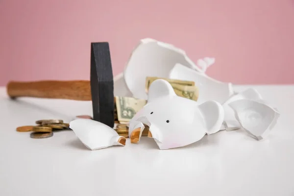 Martelo e banco piggy quebrado com dinheiro na mesa branca contra fundo de cor — Fotografia de Stock