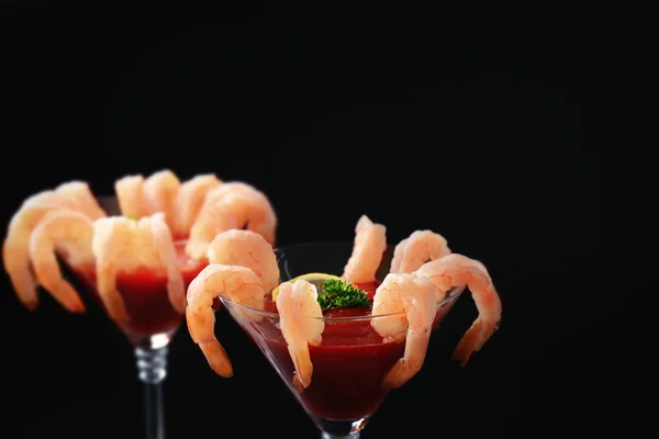 Glass with shrimp cocktail and tomato sauce on black background, closeup