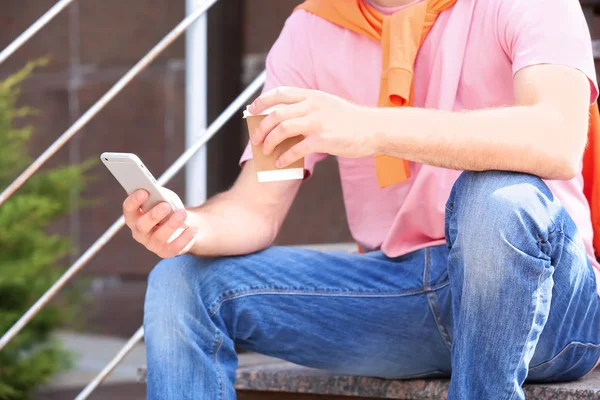 Hombre con smartphone y taza de café sentado en las escaleras al aire libre —  Fotos de Stock