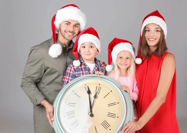 Щаслива сім'я в Санта-капелюхах з годинником на сірому фоні. Концепція зворотного відліку Різдва — стокове фото