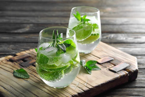 Vasos de cóctel con menta y lima sobre tabla de madera — Foto de Stock