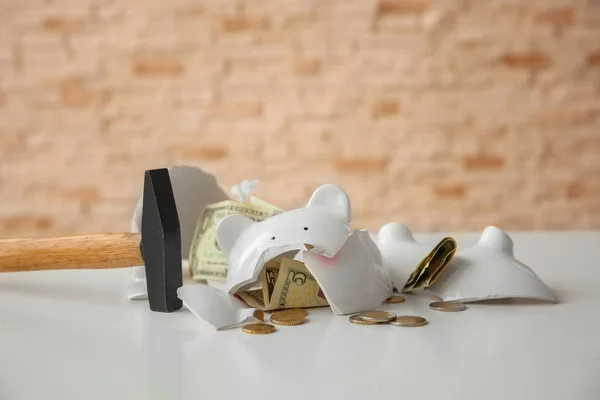 Молоток и разбитая копилка с деньгами на столе на размытом фоне — стоковое фото