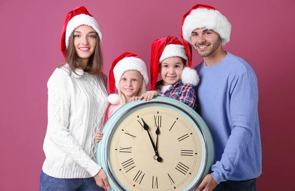 Ευτυχισμένη οικογένεια σε καπέλα Santa με το ρολόι στο χρώμα φόντου. Έννοια αντίστροφη μέτρηση Χριστουγέννων — Φωτογραφία Αρχείου