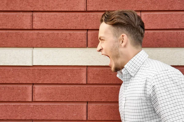 Joven hombre emocional sobre fondo de pared de ladrillo — Foto de Stock