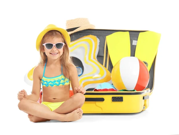 Красивая маленькая девочка сидит рядом с чемоданом на белом фоне — стоковое фото