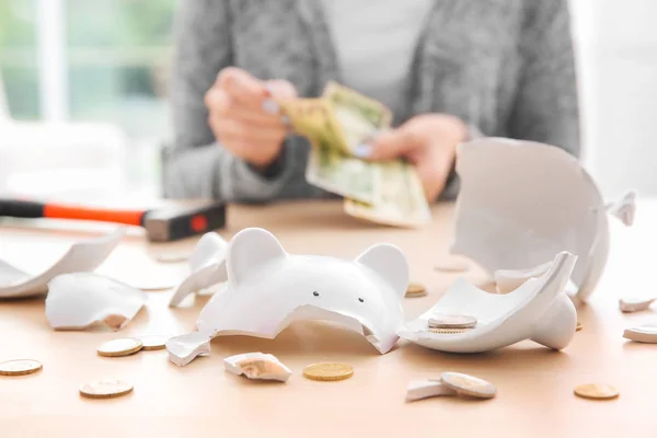 Gebroken spaarvarken met munten en wazig vrouw op achtergrond — Stockfoto