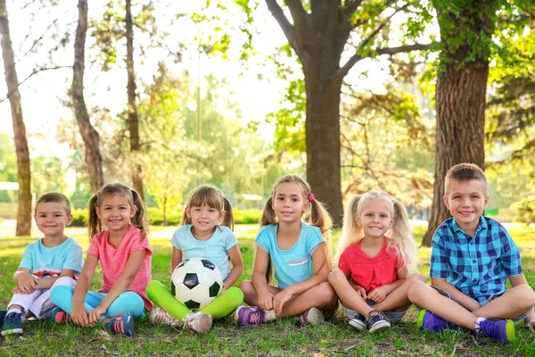 Lindos niños pequeños con pelota sentados sobre hierba verde en el parque — Foto de Stock