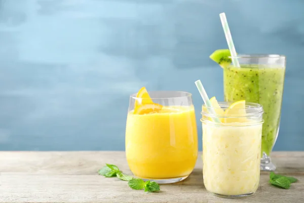 Bril met verschillende smoothies op tafel tegen een achtergrond met kleur — Stockfoto