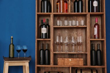 Wooden storage stand with wine bottles and glasses indoors clipart