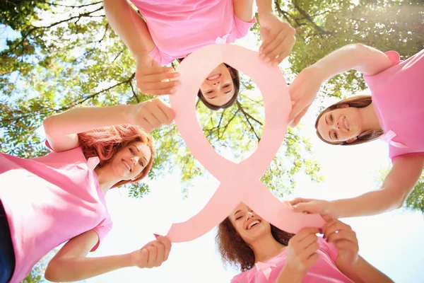Giovani donne in t-shirt rosa che tengono il nastro di consapevolezza del cancro al seno all'aperto, vista dal basso — Foto Stock