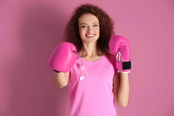 Mujer joven en camiseta rosa y guantes de boxeo sobre fondo de color. Concepto de conciencia sobre el cáncer de mama — Foto de Stock