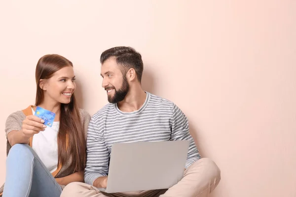 Jeune couple avec ordinateur portable et carte de crédit sur fond de couleur. Concept de magasinage Internet — Photo