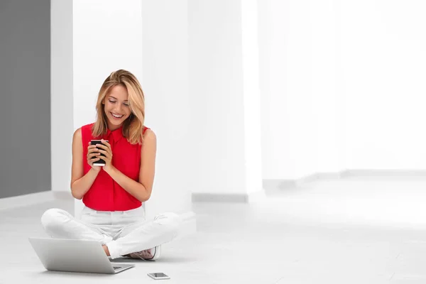 Jolie femme avec ordinateur portable moderne assis sur le sol — Photo