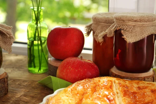 Glass jars with jam and delicious pie on windowsill — Stock Photo, Image