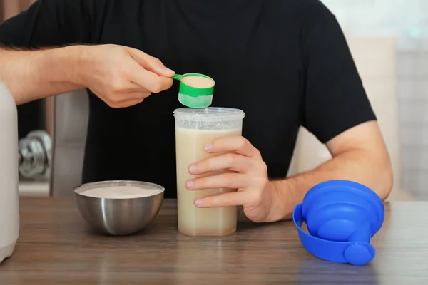 Pria menambahkan bubuk protein ke dalam botol plastik di atas meja — Stok Foto