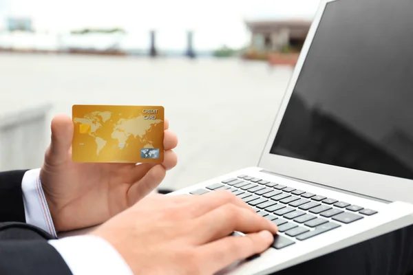 Jovem usando laptop e cartão de crédito para compras on-line, ao ar livre — Fotografia de Stock