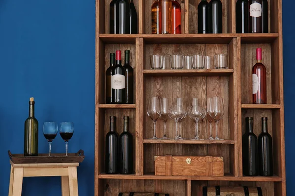 Wooden storage stand with wine bottles and glasses indoors — Stock Photo, Image