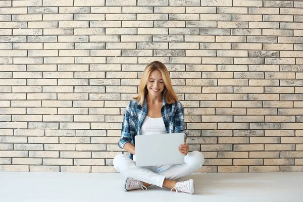 Jolie femme avec ordinateur portable moderne assis près du mur de briques — Photo