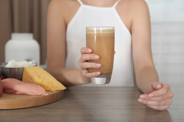 Женщина держит стакан с протеиновым коктейлем за столом — стоковое фото
